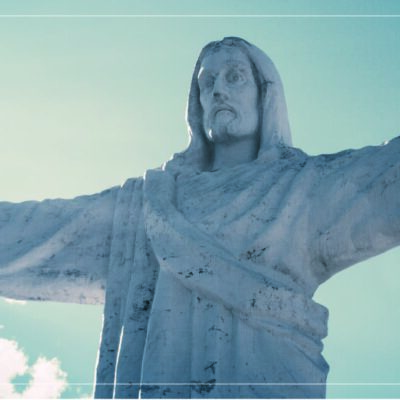 a statue of Jesus with his arms open wide in front of a blue sky with a few white clouds