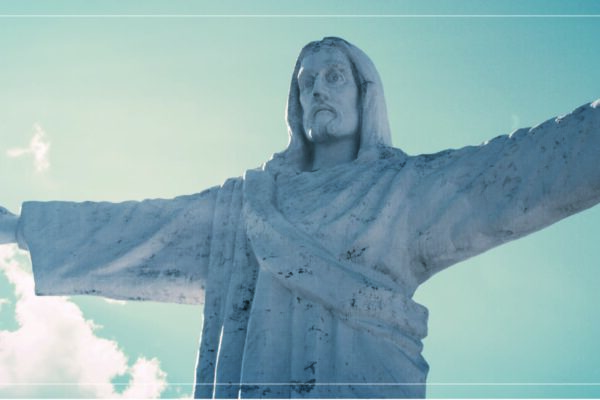 a statue of Jesus with his arms open wide in front of a blue sky with a few white clouds