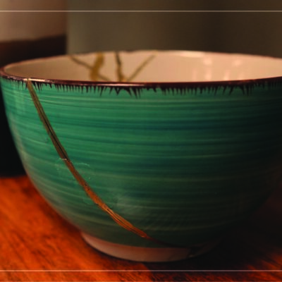 a picture of a teal ceramic bowl, repaired with gold in the Japanese traditional art of kintsugi, sitting on a wooden table