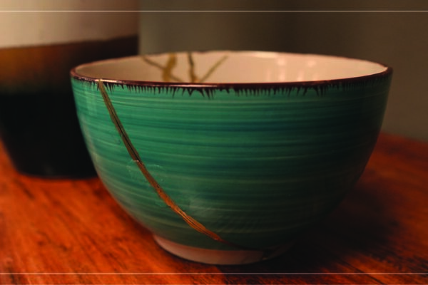 a picture of a teal ceramic bowl, repaired with gold in the Japanese traditional art of kintsugi, sitting on a wooden table